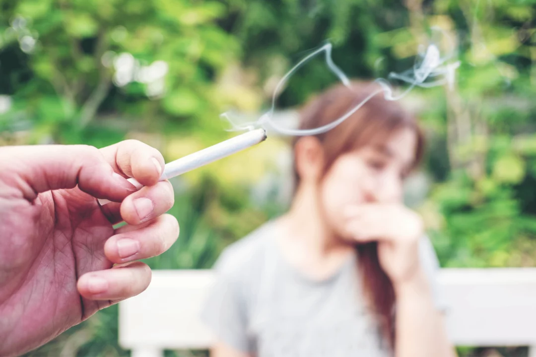 ruka v popředí drží cigaretu