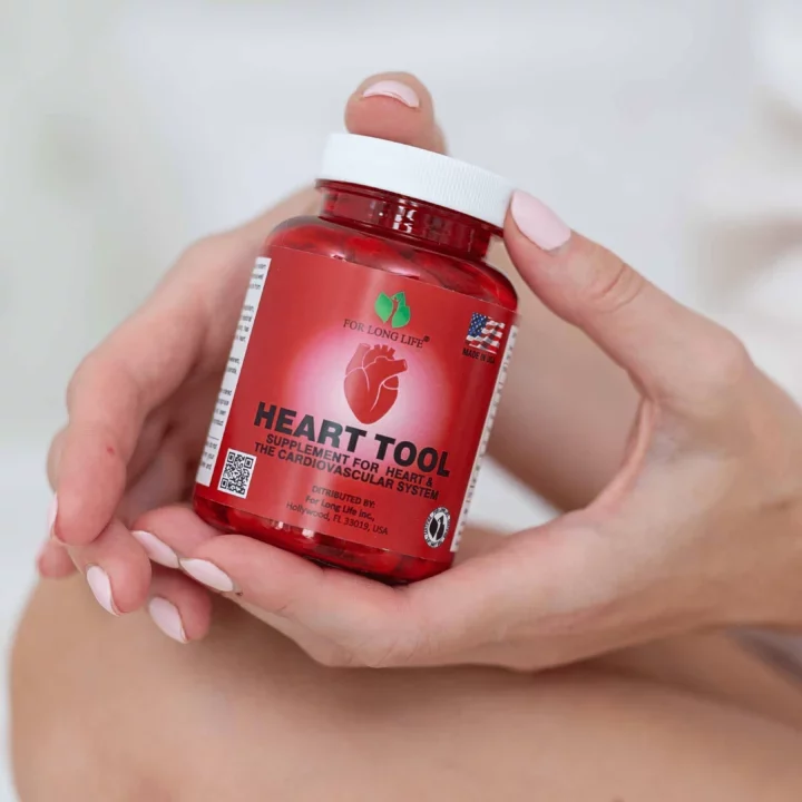 Dámské ruce drží červenou láhev doplňku stravy Heart Tool pro podporu kardiovaskulárního zdraví.