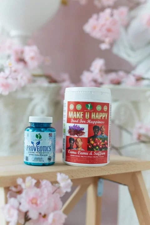 Dva doplňky stravy na stole, Proveotics probiotika a Make U Happy směs s camu camu a šafránem, květy v pozadí.