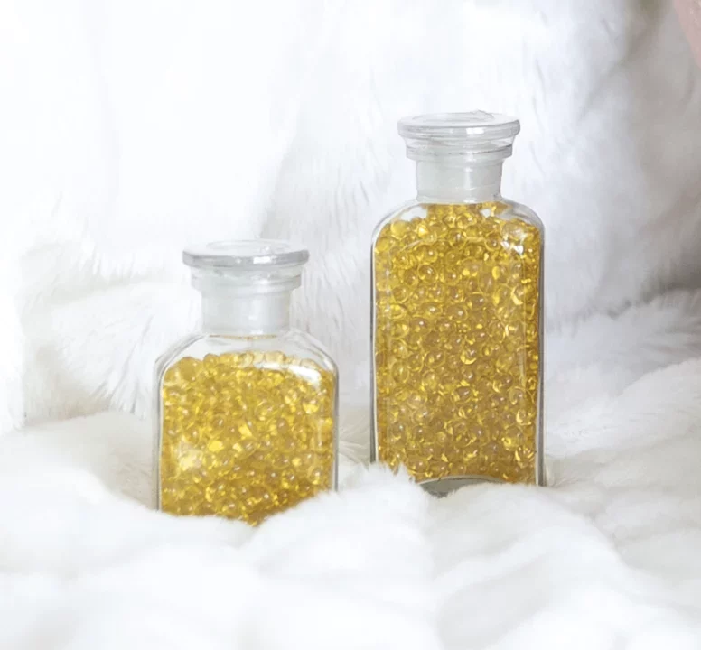 Dvě skleněné lahvičky plné zlatých perliček na bílé chlupaté textilii, dekorativní a elegantní prvek.