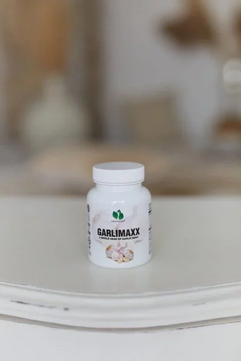 Láhev doplňku stravy Garlimaxx na bílém stole, podporující zdraví díky obsahu česneku.