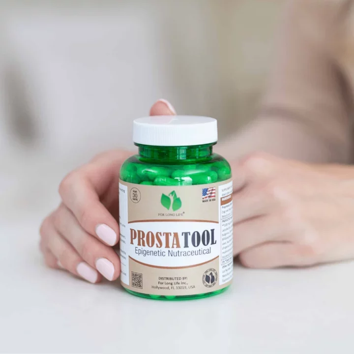 Zelená lahvička s nápisem PROSTATOOL, epigenetický nutriční doplněk, v ženských rukou na bílém pozadí.