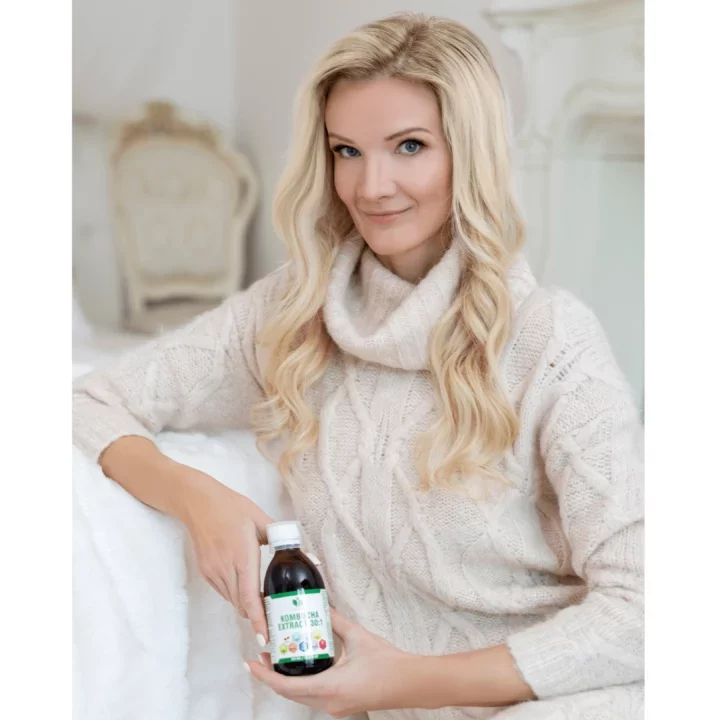 Žena v béžovém svetru držící lahvičku s kombo extraktem, sedící v elegantním interiéru s bílými detaily.