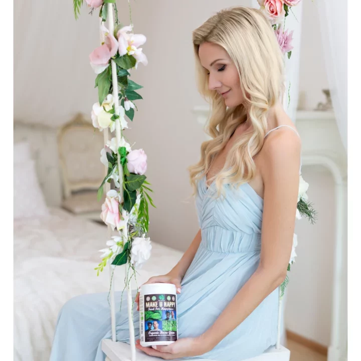 Žena v modrých šatech sedí na houpačce zdobené květinami a drží nádobu s doplňkem stravy Make U Happy.