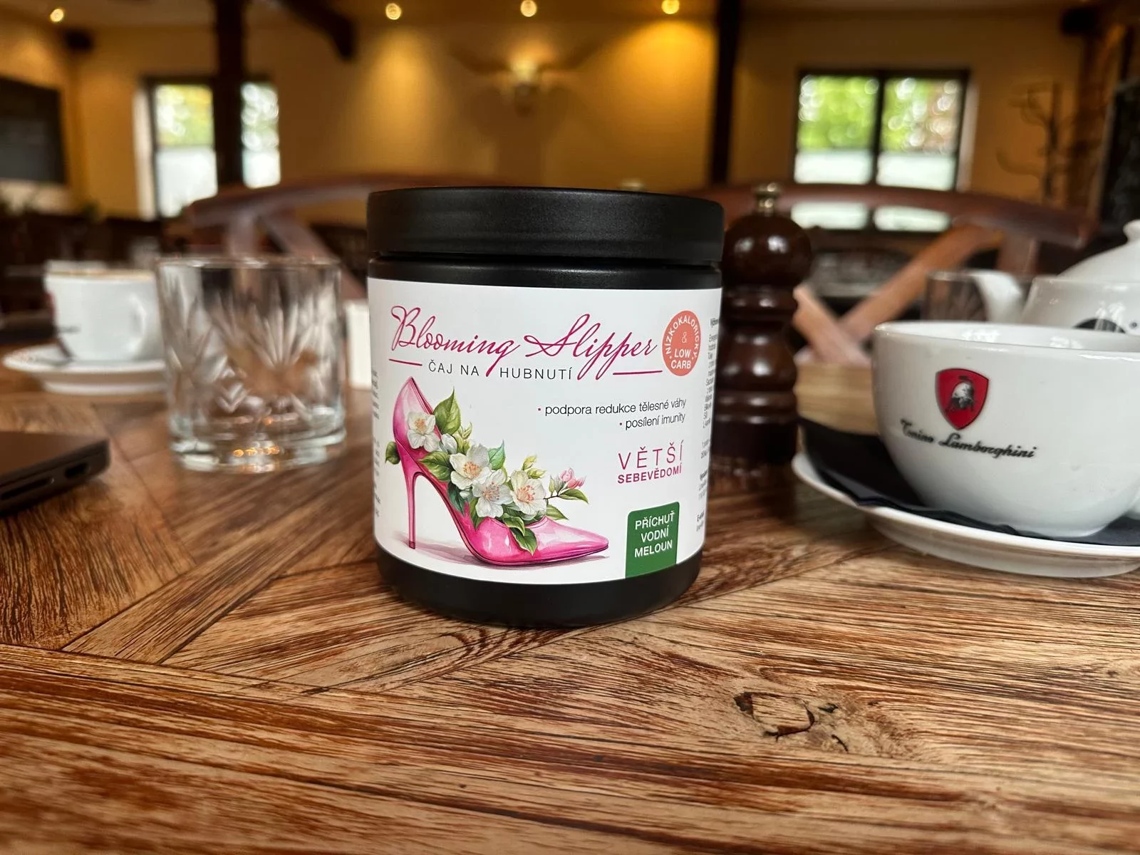 Sklenice čaje na hubnutí Blooming Slipper s příchutí vodního melounu, umístěná na dřevěném stole v útulné kavárně.