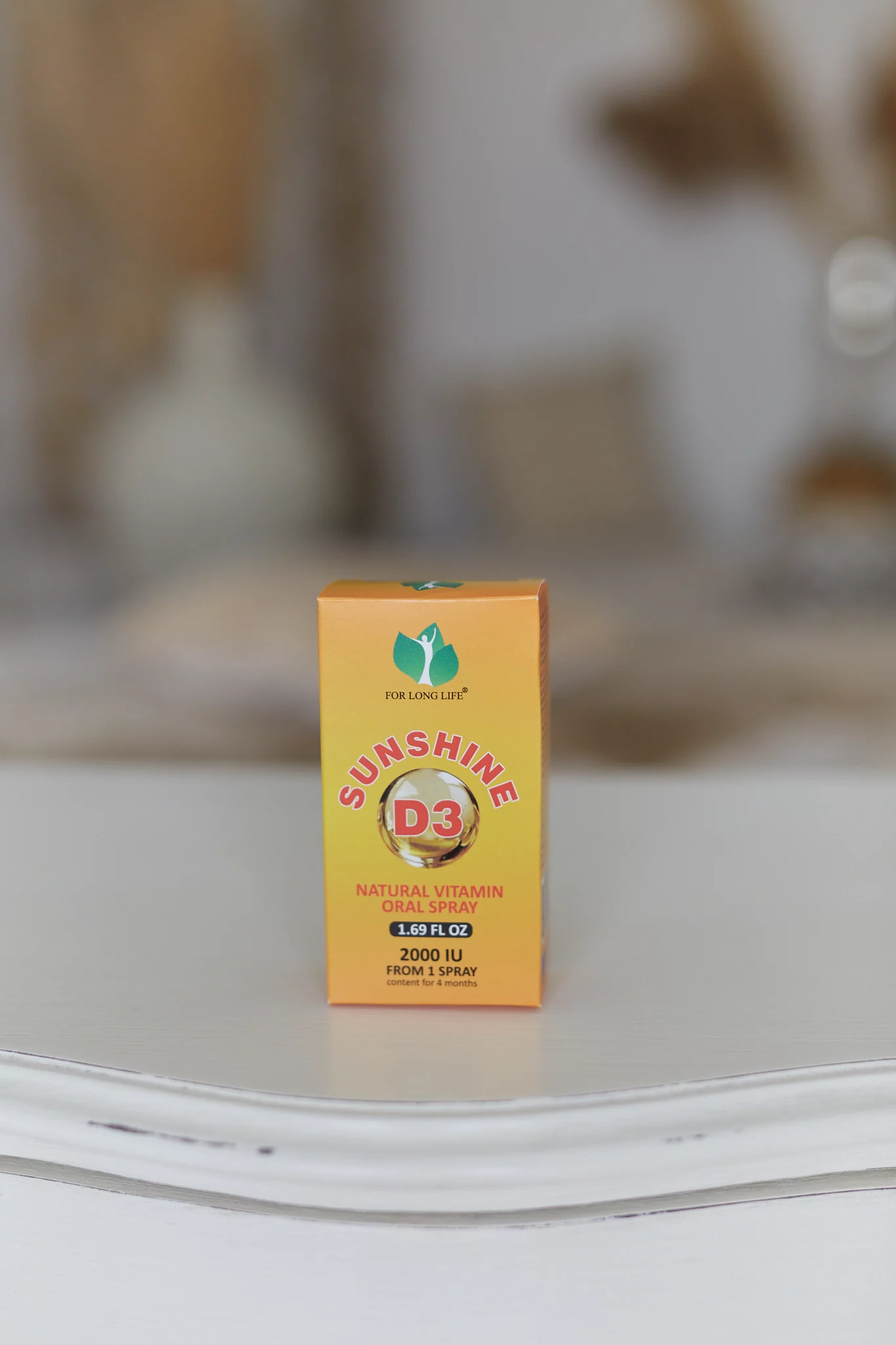 Jasně zbarvená oranžová krabička perorálního spreje s vitamínem D3 s označením „Sunshine D3“ s podrobnostmi o dávkování a velikosti obsahu.